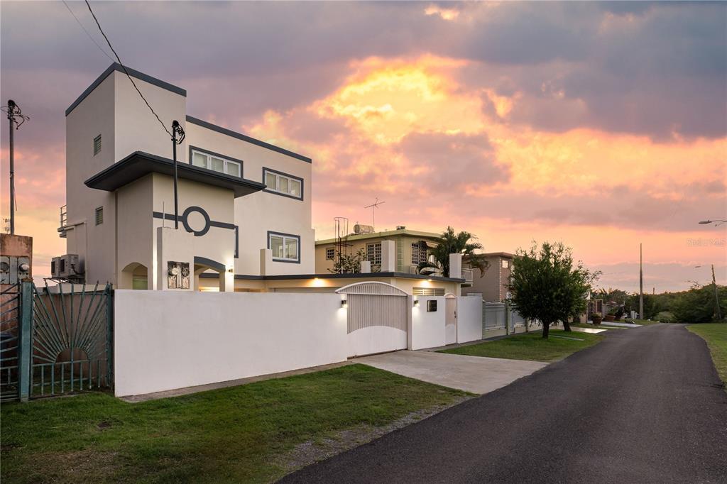 A modern three-story house with a white exterior wall and gated driveway at sunset — SR 307 km 7.9 Boqueron VILLA NAUTICA, UNION ST, JOSE ST BEACH Lot # 2, BOQUERON, PR