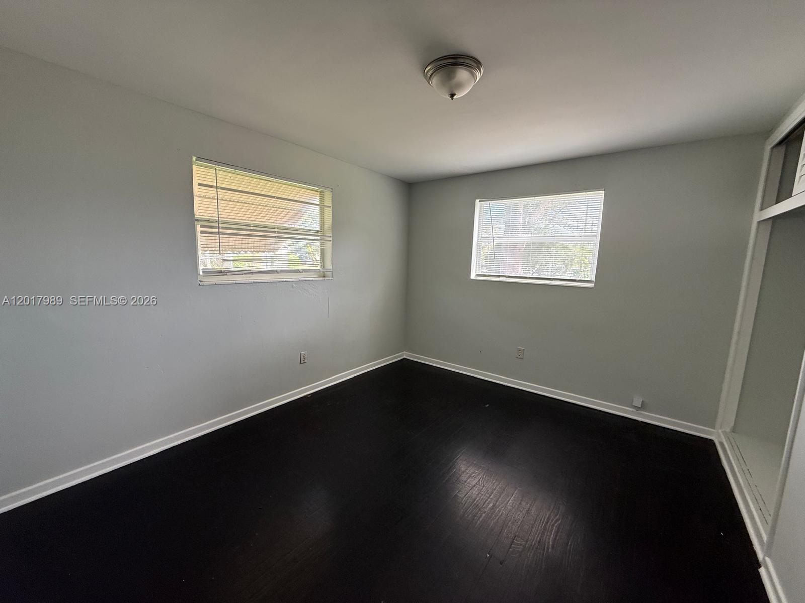 An empty bedroom features light gray walls, dark wood flooring, and two windows with blinds — 4393 Davis Rd # 1, Lake Worth FL 33461, LAKE WORTH, FL