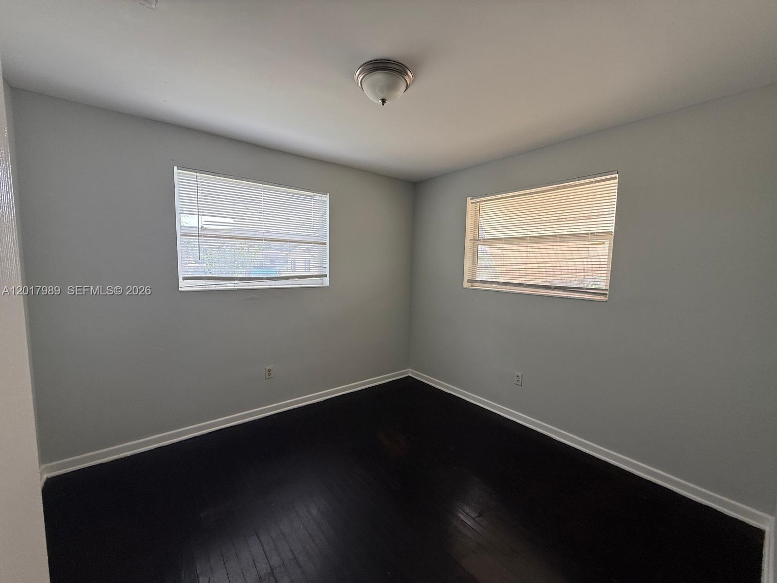 An empty room features light gray walls, dark wood flooring, and two windows with blinds — 4393 Davis Rd # 1, Lake Worth FL 33461, LAKE WORTH, FL