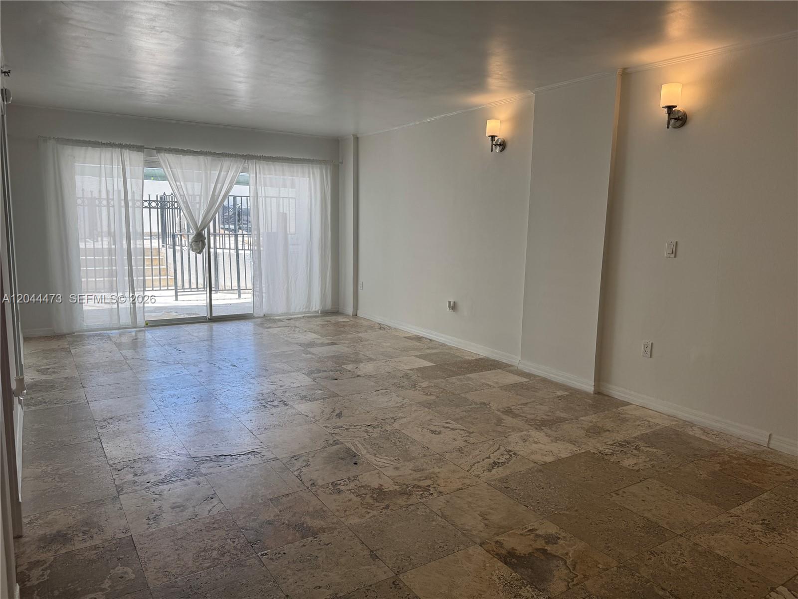 An empty room features large stone floor tiles, white walls, wall sconces, and sliding glass doors — 1345 West Ave # 202, Miami Beach FL 33139, MIAMI BEACH, FL
