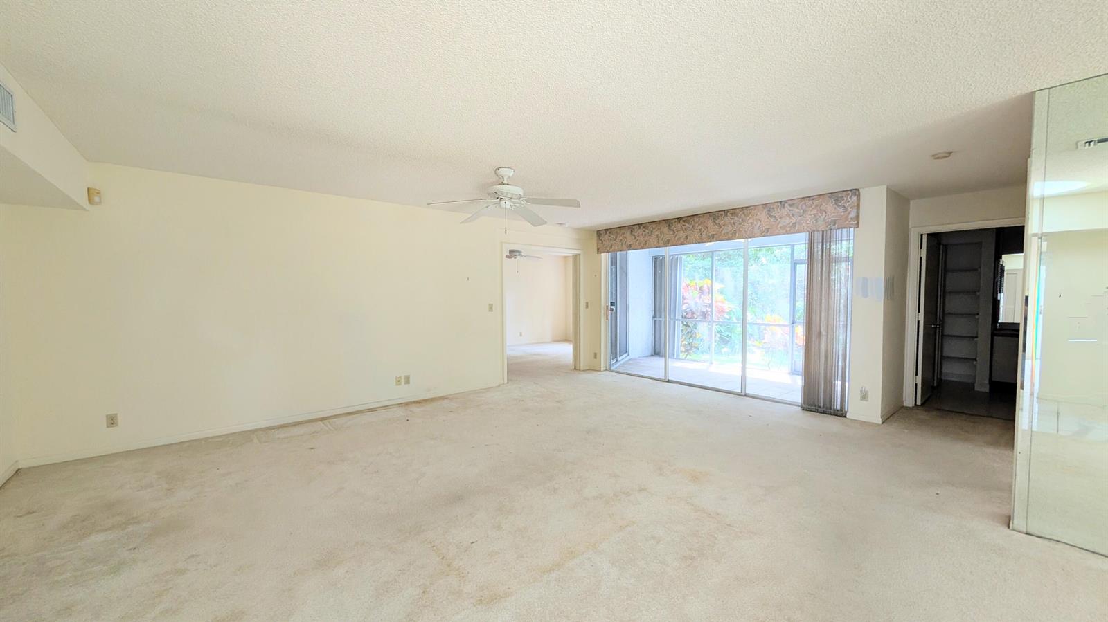 An empty living room features beige carpet, a ceiling fan, and sliding glass patio doors — 9746 Nickels Boulevard # 104, Boynton Beach FL 33436, BOYNTON BEACH, FL