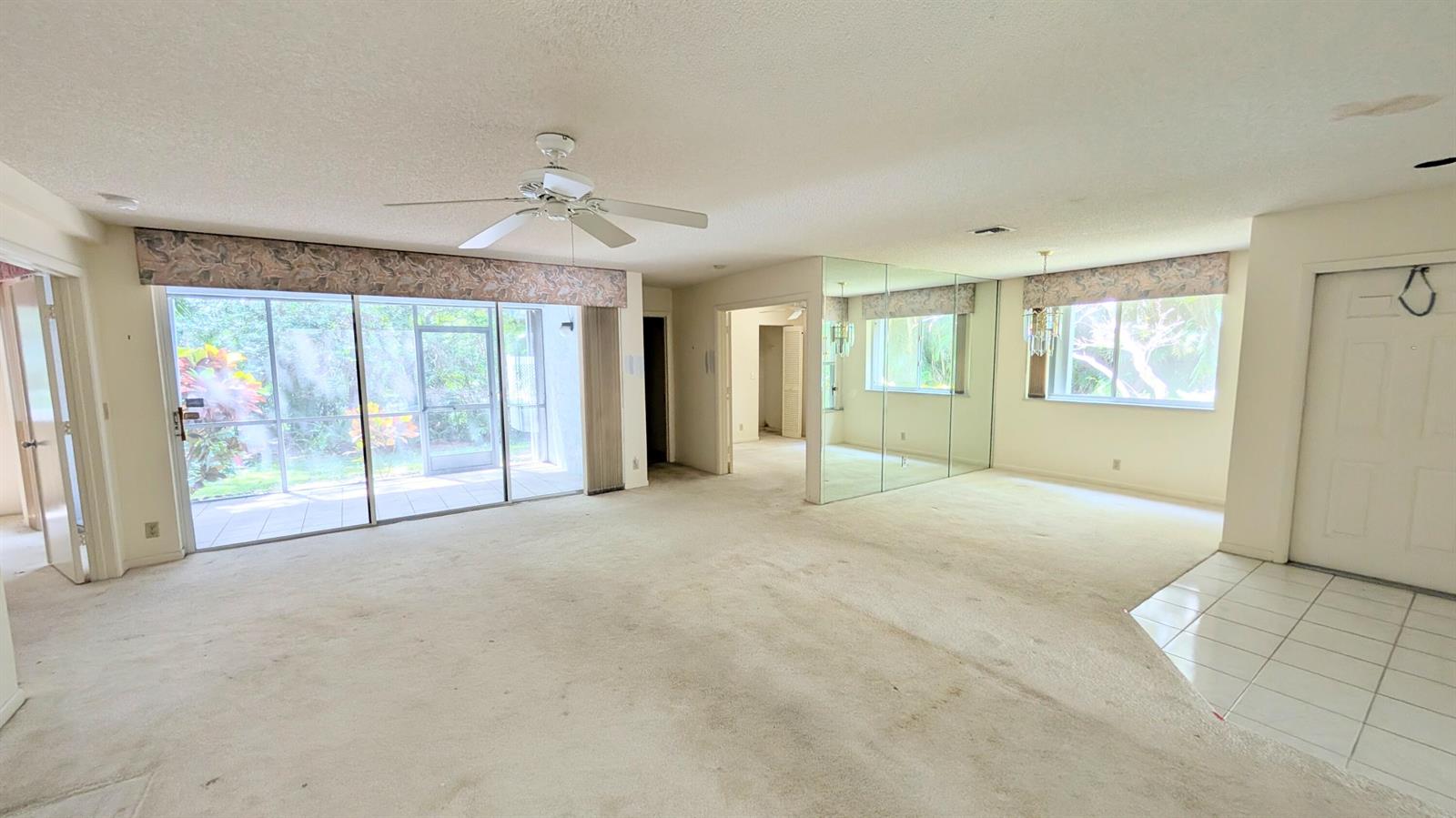 A living room with beige carpet, mirrored walls, a ceiling fan, and sliding glass doors — 9746 Nickels Boulevard # 104, Boynton Beach FL 33436, BOYNTON BEACH, FL