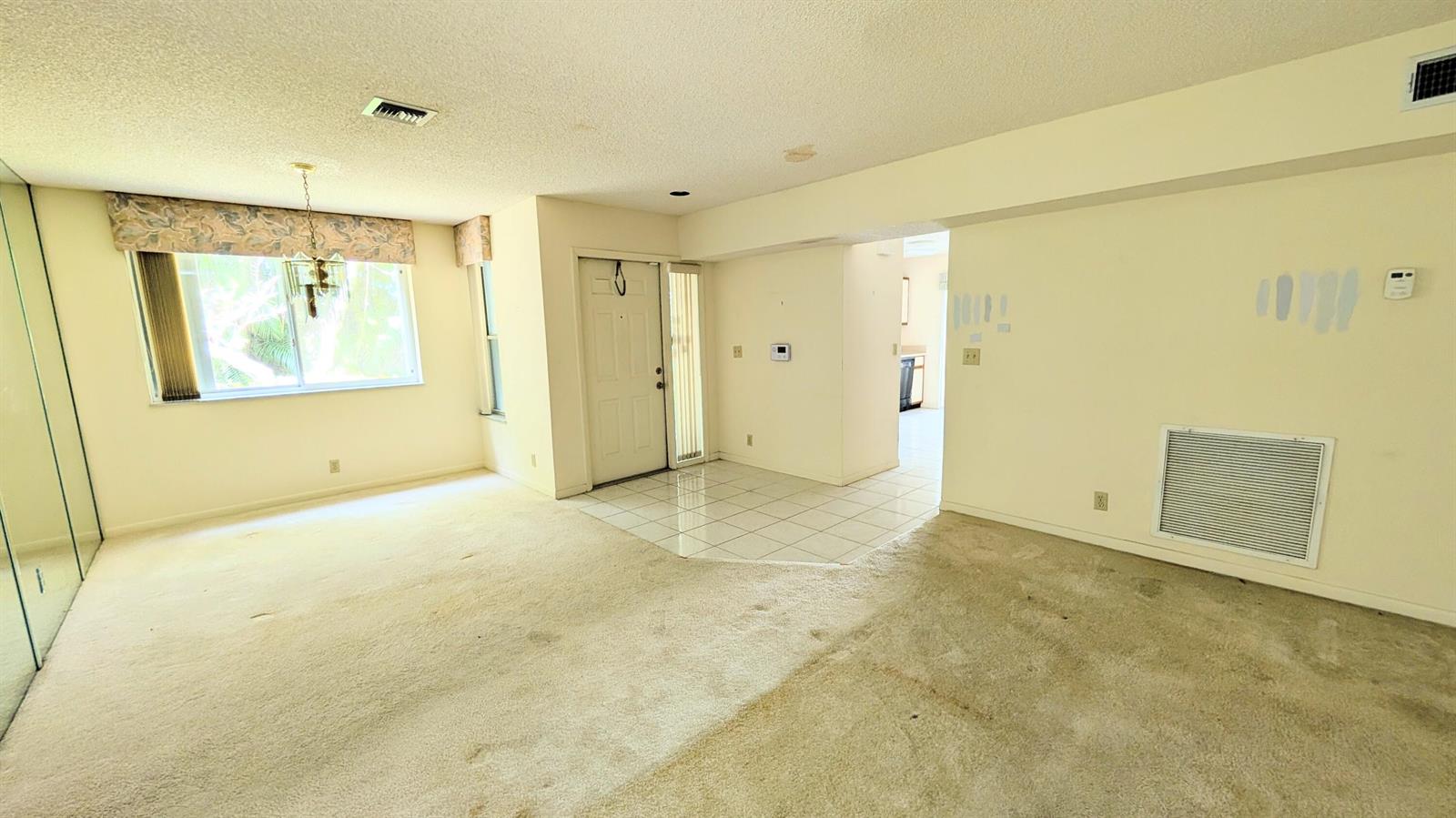 A living room with beige carpet, a tiled entryway, a white front door, and windows — 9746 Nickels Boulevard # 104, Boynton Beach FL 33436, BOYNTON BEACH, FL