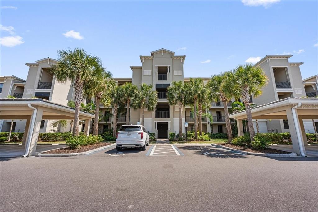 A multi-story apartment building with palm trees and covered parking spaces in front — 18114 GAWTHROP DRIVE UNIT 304, BRADENTON, FL