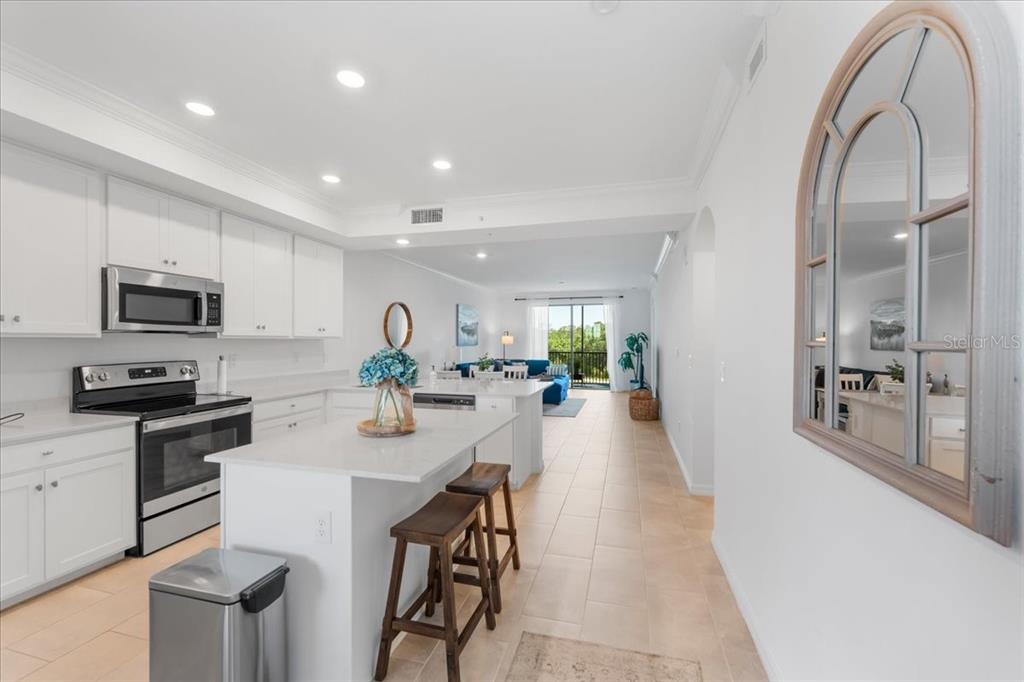 A bright kitchen features white cabinets, a central island with bar stools, and tile flooring — 18114 GAWTHROP DRIVE UNIT 304, BRADENTON, FL