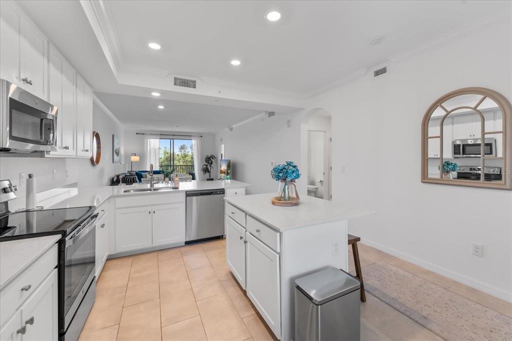 A white kitchen with an island, stainless steel appliances, and tile flooring opens to living — 18114 GAWTHROP DRIVE UNIT 304, BRADENTON, FL