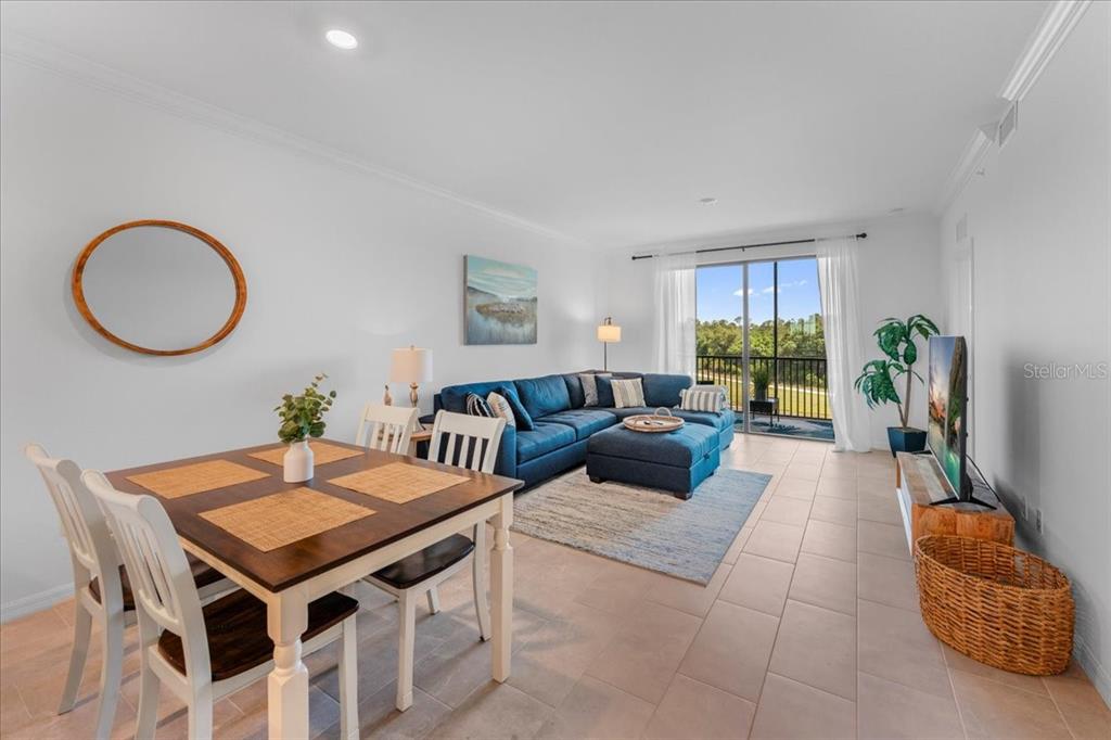 A bright living and dining area features tile floors, a blue sectional, and balcony access — 18114 GAWTHROP DRIVE UNIT 304, BRADENTON, FL