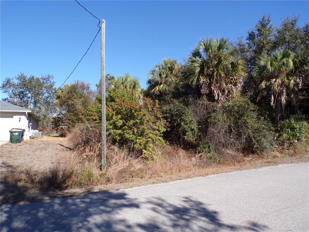 A vacant, overgrown lot sits next to a house with a utility pole in front — BENNETT LANE, NORTH PORT, FL