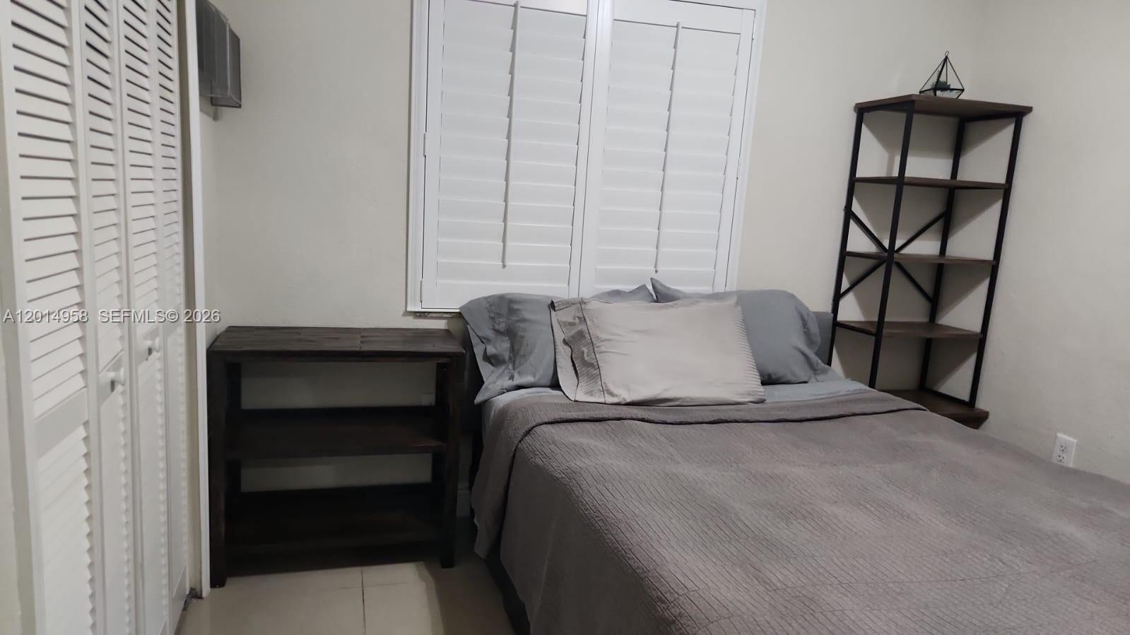 A bedroom features a bed with gray bedding, a wooden side table, and a tall shelf — 1935 NW 96th St, Miami FL 33147, MIAMI, FL