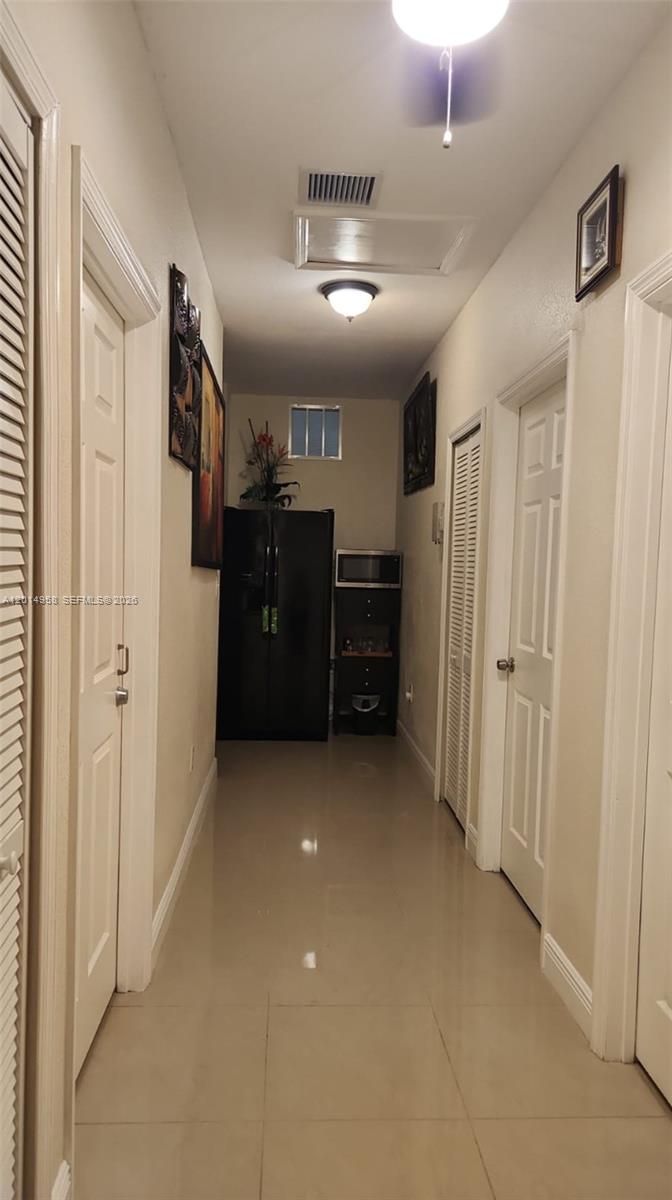 A narrow hallway features light tile flooring, white doors, and a black refrigerator at the end — 1935 NW 96th St, Miami FL 33147, MIAMI, FL