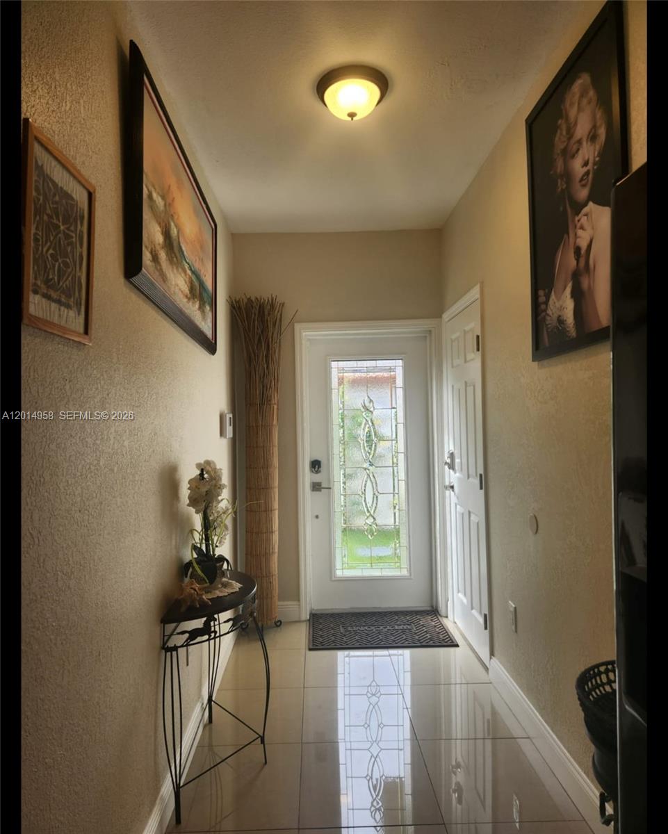 An entryway features a glass-paneled front door, tile flooring, wall art, and a console table — 1935 NW 96th St, Miami FL 33147, MIAMI, FL