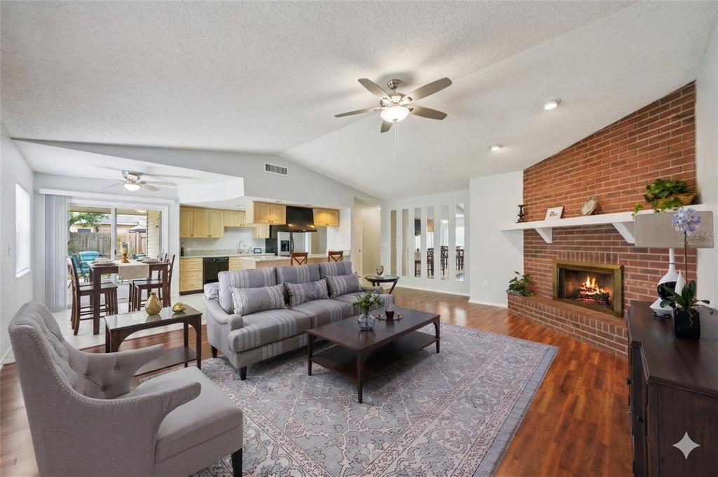 A living room with a brick fireplace, wood-look flooring, a ceiling fan, and sliding glass doors — 105 LOTUS CIRCLE, SAFETY HARBOR, FL