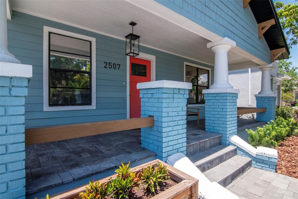 A blue house exterior features a red front door, brick porch columns, and stone steps — 2507 W GRAY STREET, TAMPA, FL