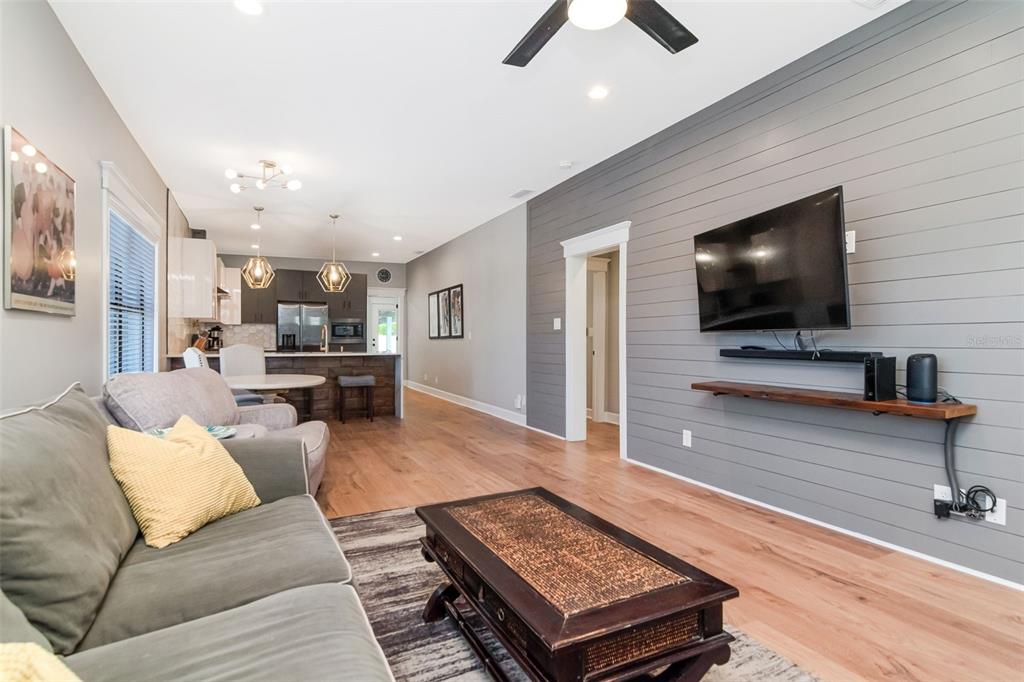 A living room with wood flooring, a gray shiplap accent wall, and an open kitchen — 2507 W GRAY STREET, TAMPA, FL