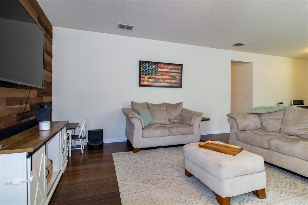 A living room features a wood-paneled accent wall, beige sofas, and a white media console — 408 CEDAR GLEN DRIVE, LAKE ALFRED, FL