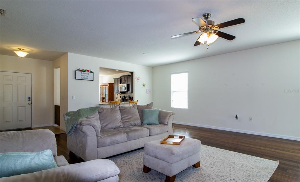 A living room with a grey sofa, ottoman, ceiling fan, and hardwood floors — 408 CEDAR GLEN DRIVE, LAKE ALFRED, FL