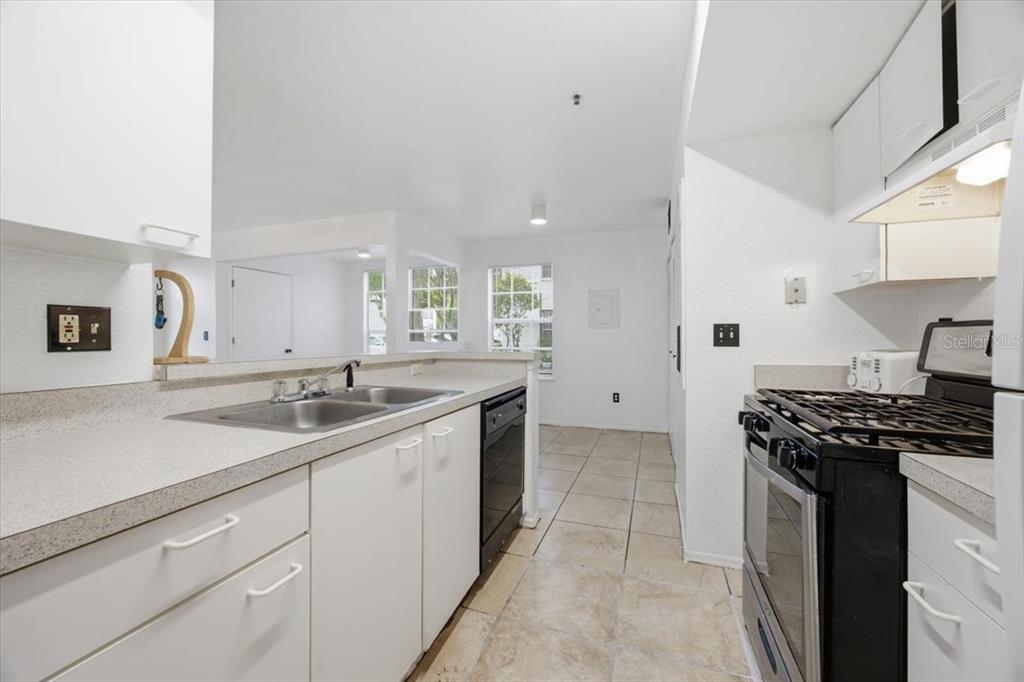 A kitchen with white cabinets, a black stove, and a double sink overlooks a dining area — 1602 COLUMBIA ARMS CIRCLE UNIT 106, KISSIMMEE, FL