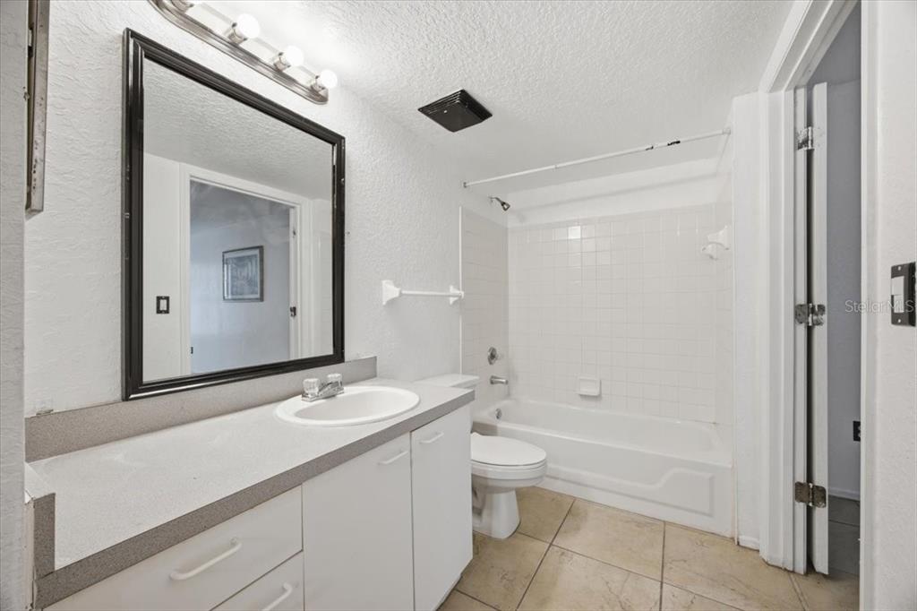 A bathroom features a white vanity, a mirror, a toilet, and a tiled shower-tub combo — 1602 COLUMBIA ARMS CIRCLE UNIT 106, KISSIMMEE, FL