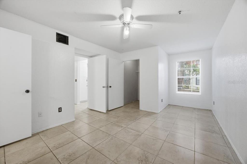 A bedroom with white walls, tiled floors, a ceiling fan, and two open doorways — 1602 COLUMBIA ARMS CIRCLE UNIT 106, KISSIMMEE, FL
