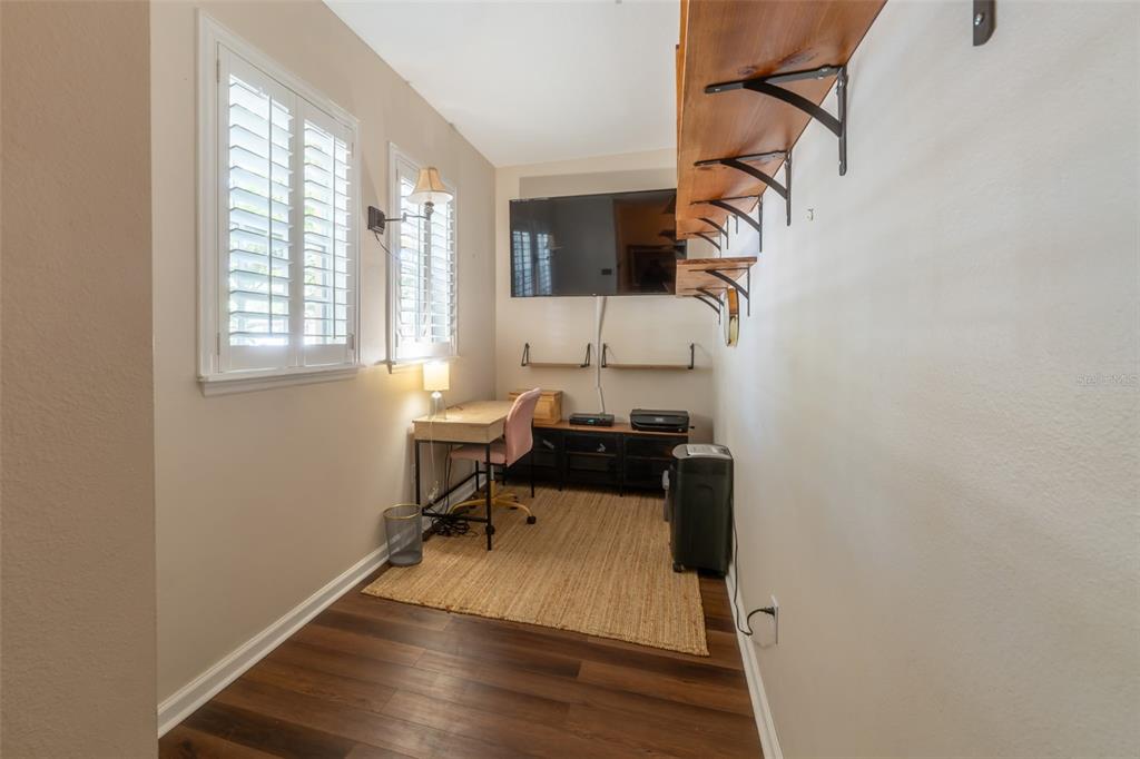 A small home office features wood-look flooring, a desk, a wall-mounted television, and open shelving — 815 S FORT HARRISON AVENUE, CLEARWATER, FL