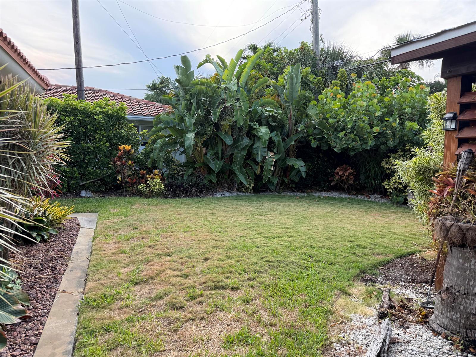 A grassy backyard features lush tropical landscaping, a concrete border, and a wooden patio structure — 1140 Morse Boulevard, Singer Island FL 33404, SINGER ISLAND, FL