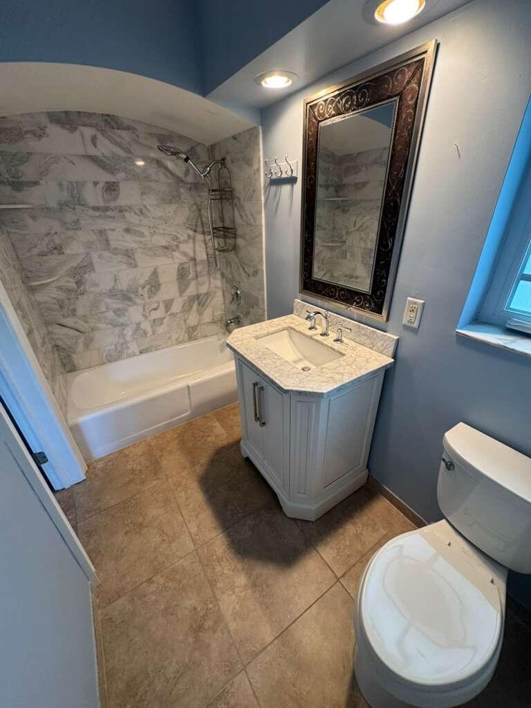 A bathroom featuring a marble-tiled shower-tub combo, a white vanity, and light blue walls — 1140 Morse Boulevard, Singer Island FL 33404, SINGER ISLAND, FL