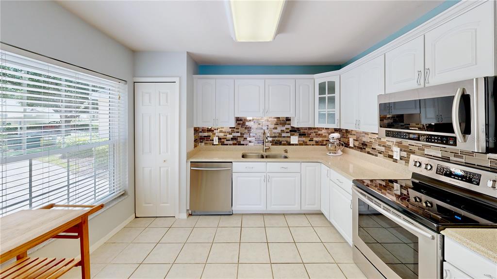 A kitchen features white cabinets, stainless steel appliances, a tiled backsplash, and light-colored floor tiles — 2067 BRAXTON STREET, CLERMONT, FL