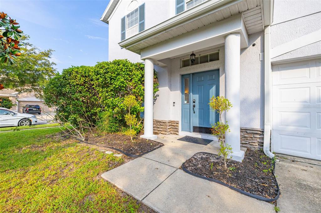 The exterior of a house features a blue front door, white columns, and landscaping — 1404 SWAINSON COURT, ORLANDO, FL