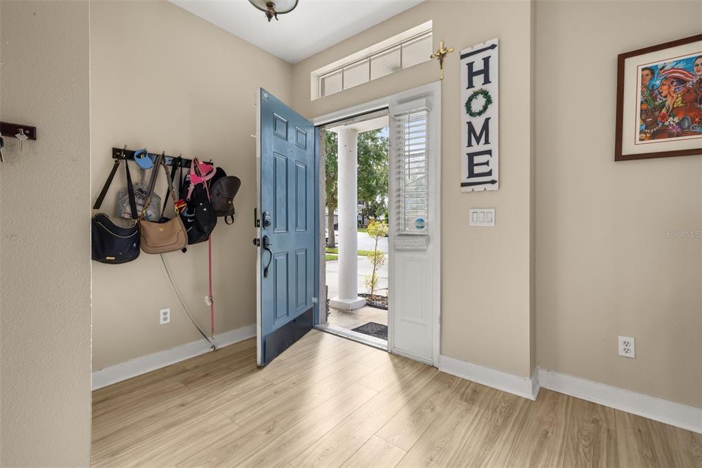 An entryway features light wood-look flooring, a blue front door, and a wall-mounted coat rack — 1404 SWAINSON COURT, ORLANDO, FL
