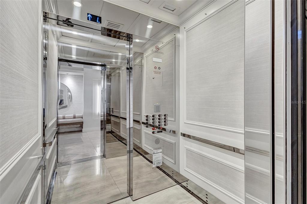 A modern elevator interior features mirrored walls, white paneled wainscoting, and a digital floor indicator — 3060 GRAND BAY BOULEVARD UNIT 174, LONGBOAT KEY, FL