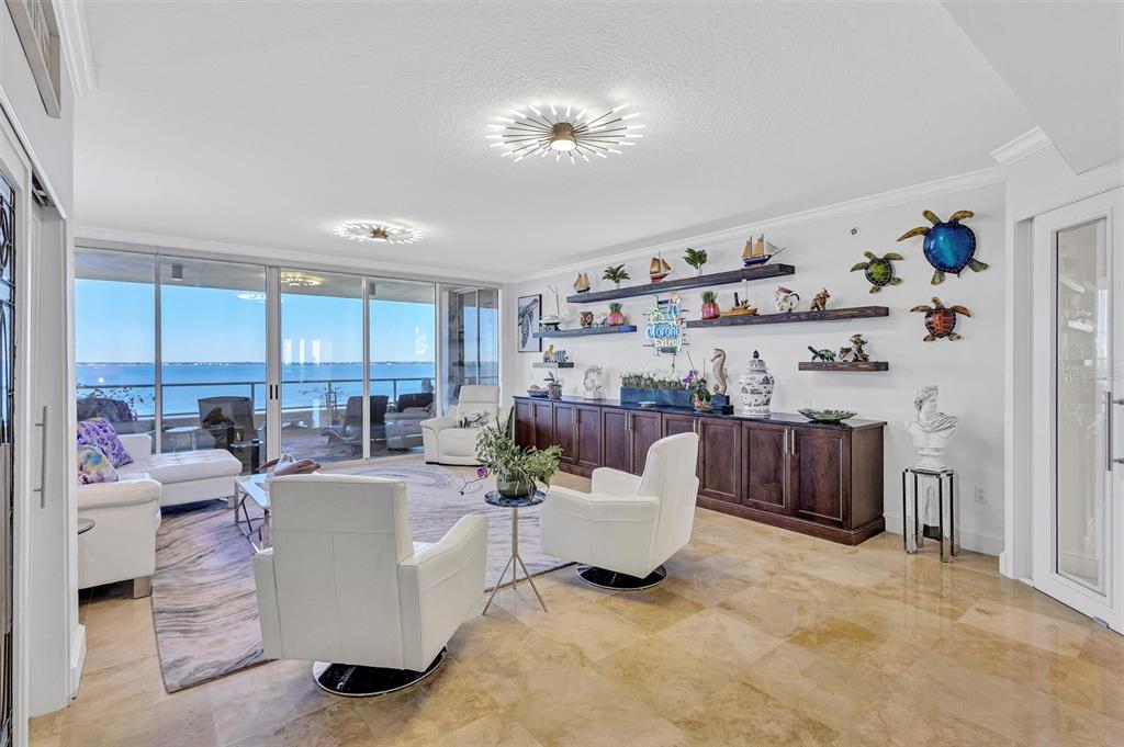 A bright living room features white leather furniture, dark wood cabinetry, and a waterfront view — 3060 GRAND BAY BOULEVARD UNIT 174, LONGBOAT KEY, FL