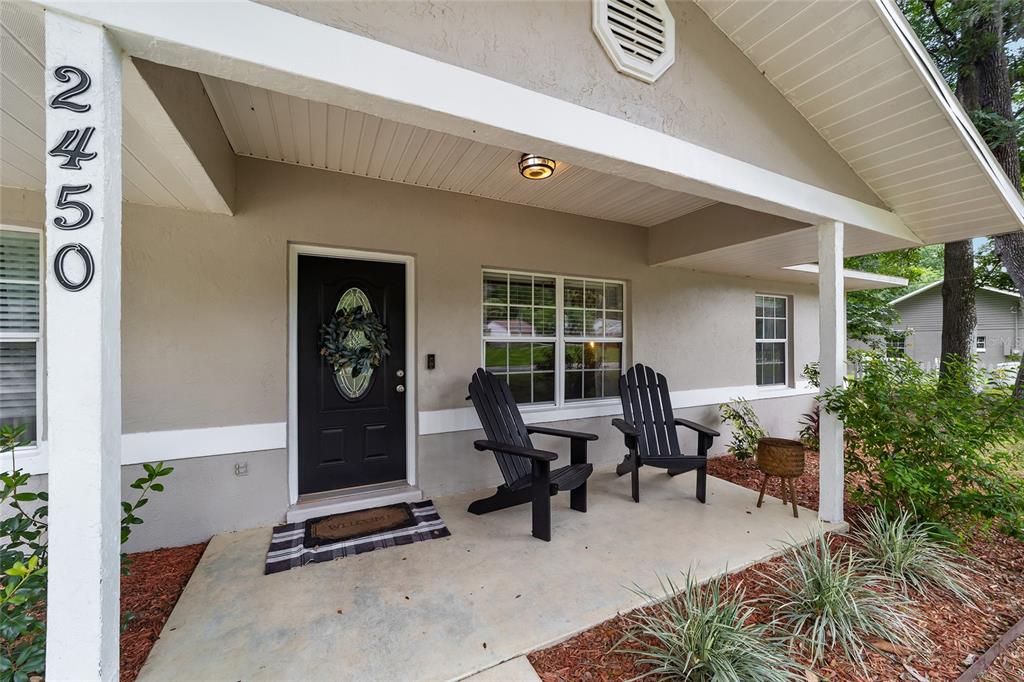 A covered front porch features two black Adirondack chairs, a welcome mat, and a door — 2450 SE 40TH STREET ROAD, OCALA, FL