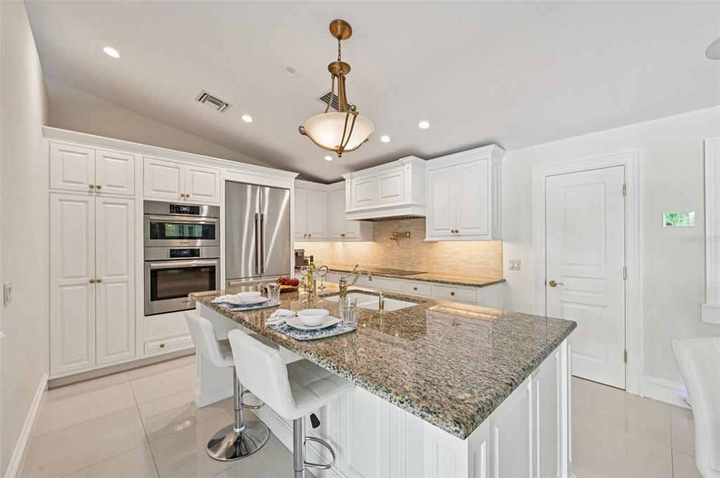 A kitchen features white cabinetry, granite countertops, a center island with bar seating, and appliances — 1121 MORNINGSIDE PLACE, SARASOTA, FL