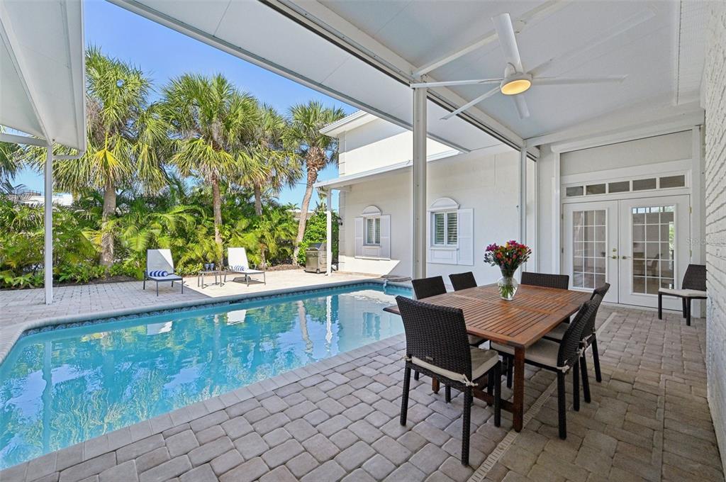 A covered brick patio features a dining set, a swimming pool, and tropical landscaping — 1121 MORNINGSIDE PLACE, SARASOTA, FL
