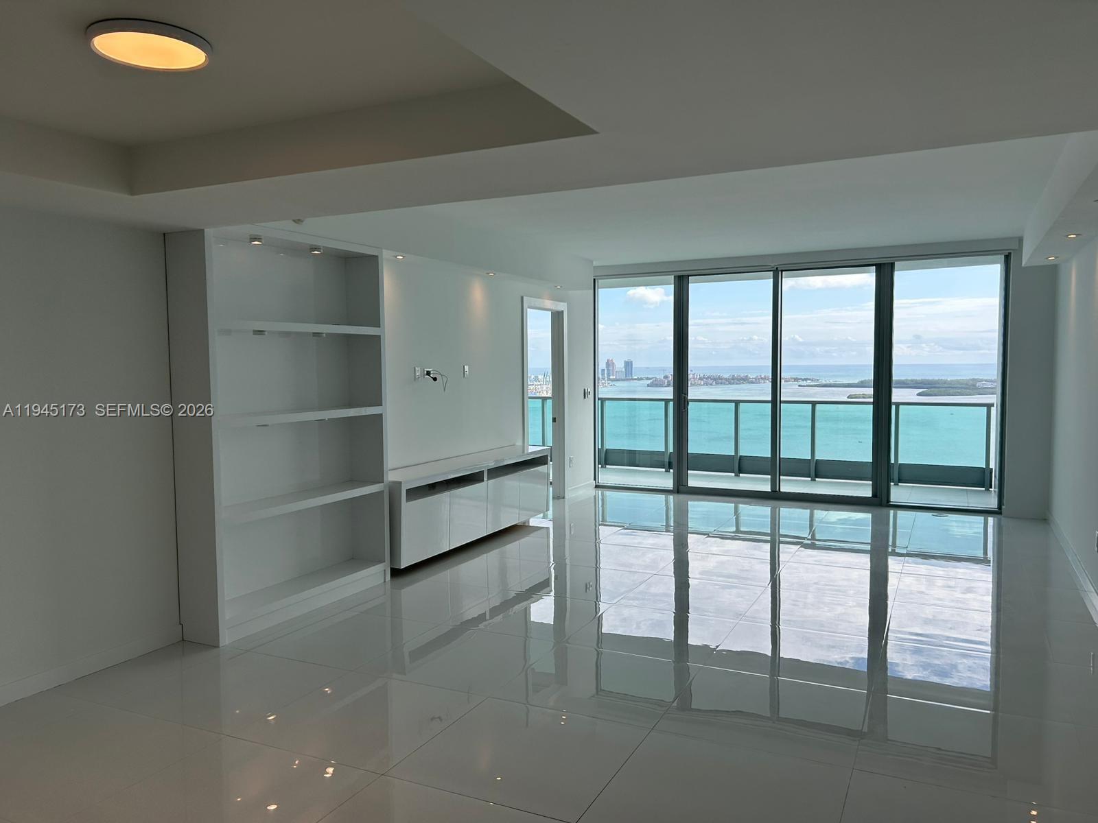A bright living area features white tile floors, built-in shelving, and floor-to-ceiling windows overlooking water — 1331 Brickell Bay Dr # 4107, Miami FL 33131, MIAMI, FL