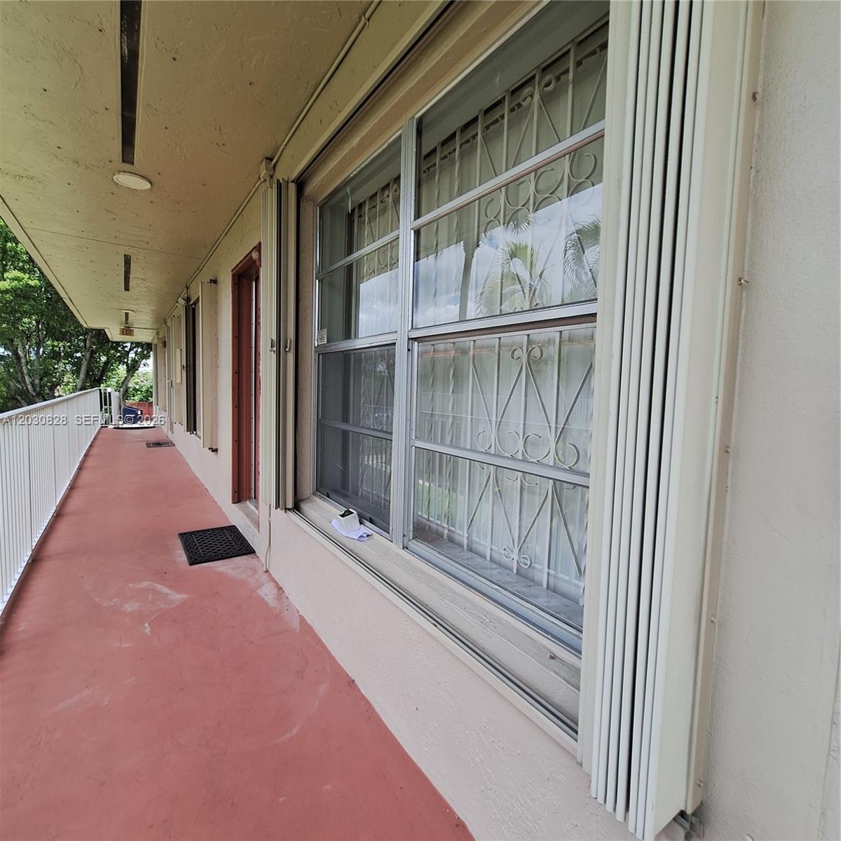An exterior walkway with red flooring, a white railing, and windows with security bars — 12850 SW 43rd Dr # B, Miami FL 33175, MIAMI, FL