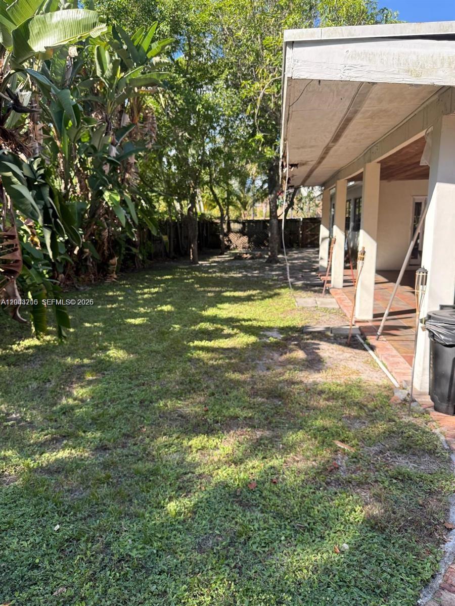 A grassy backyard features a covered patio area with tiled flooring and mature trees — 5600 SW 74th Ct, Miami FL 33143, MIAMI, FL
