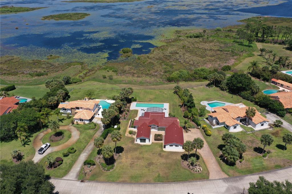 An aerial view shows three houses with swimming pools situated along a large lake — 13300 SKIING PARADISE BOULEVARD, CLERMONT, FL