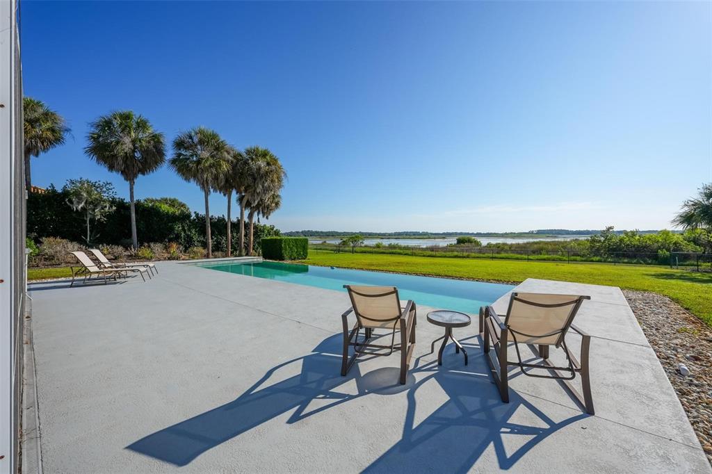 A concrete pool deck features lounge chairs overlooking an infinity pool and a grassy landscape — 13300 SKIING PARADISE BOULEVARD, CLERMONT, FL