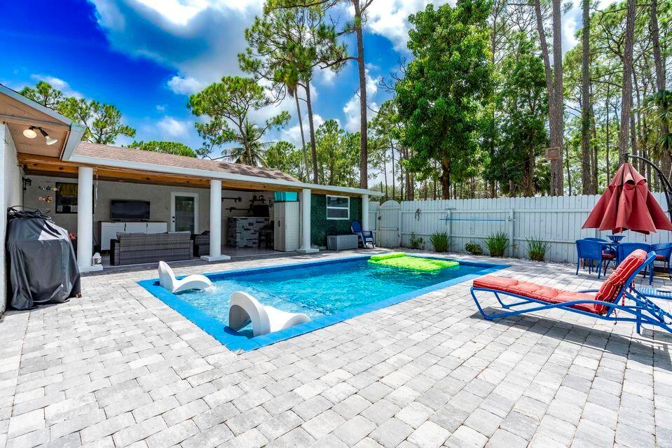 A backyard features a rectangular swimming pool with lounge chairs on a paved patio — 15211 60th Place N, Loxahatchee FL 33470, LOXAHATCHEE, FL
