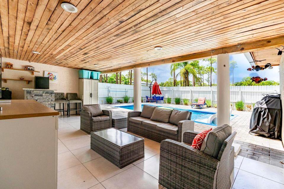 A covered outdoor patio features a wood-paneled ceiling, wicker furniture, and a swimming pool — 15211 60th Place N, Loxahatchee FL 33470, LOXAHATCHEE, FL