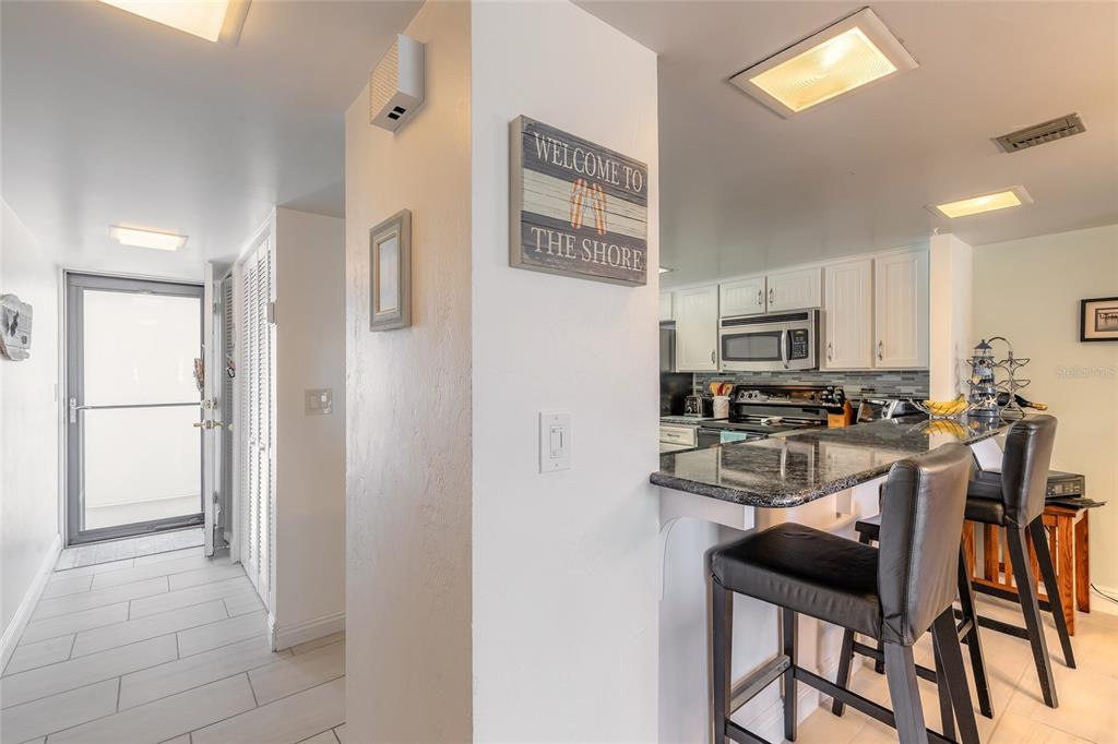 A kitchen with a granite breakfast bar and stools sits next to a hallway entrance — 2626 S ATLANTIC AVENUE UNIT 3020, DAYTONA BEACH SHORES, FL