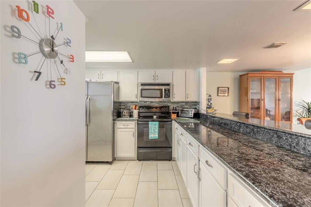 A kitchen features white cabinetry, dark granite countertops, stainless steel appliances, and a colorful wall clock — 2626 S ATLANTIC AVENUE UNIT 3020, DAYTONA BEACH SHORES, FL