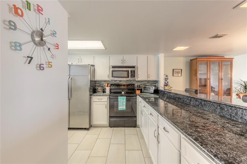 A kitchen features white cabinets, dark granite countertops, stainless steel appliances, and tile flooring — 2626 S ATLANTIC AVENUE UNIT 3020, DAYTONA BEACH SHORES, FL