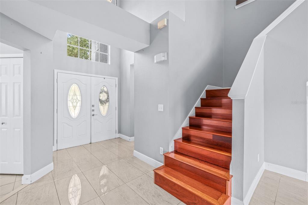 A foyer features a high ceiling, tile flooring, double front doors, and a wooden staircase — 2239 MALLORY CIRCLE, HAINES CITY, FL