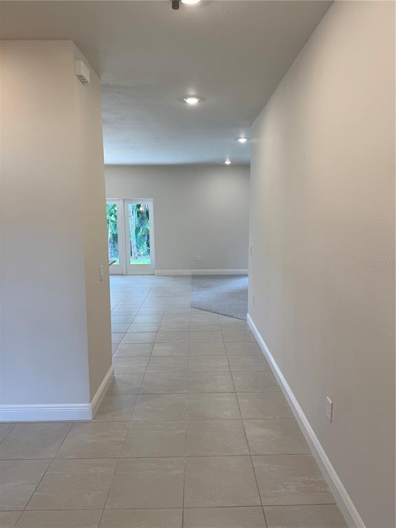 A hallway with light-colored tile flooring leads toward a room with carpet and glass doors — 3271 NADASKY AVENUE, NORTH PORT, FL