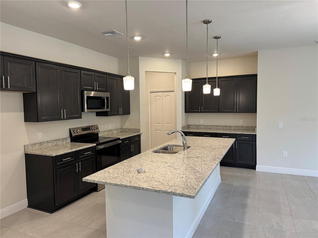 A kitchen features dark wood cabinets, granite countertops, a central island, and stainless steel appliances — 3271 NADASKY AVENUE, NORTH PORT, FL