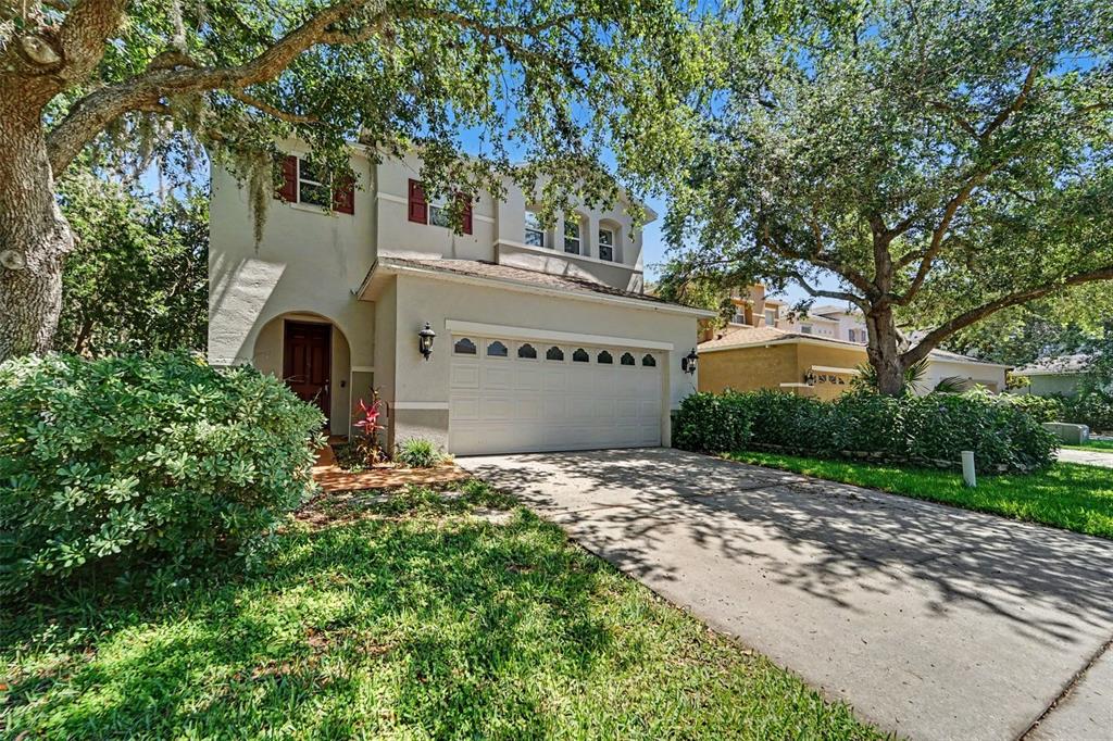 A two-story house with a beige stucco exterior, a two-car garage, and mature trees — 2436 SPRING HOLLOW LOOP, WESLEY CHAPEL, FL