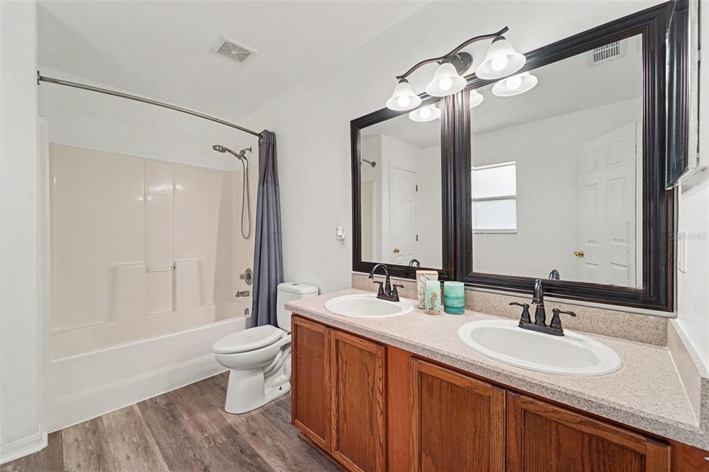 A bathroom features a double vanity with wood cabinets, a mirror, and a shower-tub combo — 2436 SPRING HOLLOW LOOP, WESLEY CHAPEL, FL