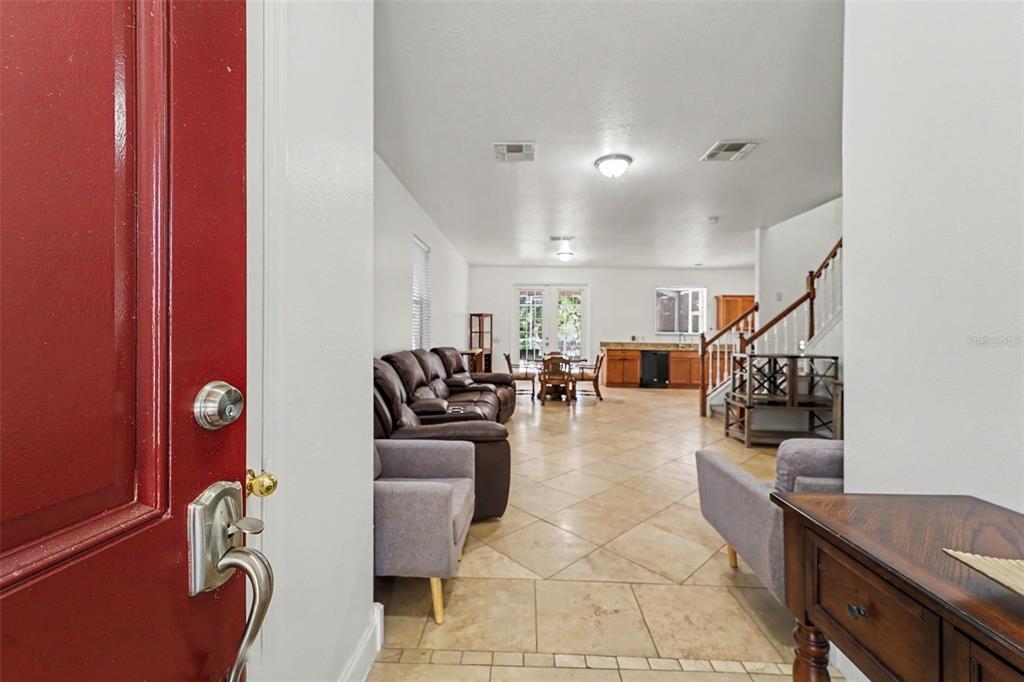 A view from a red front door into an open-concept living room with tiled floors — 2436 SPRING HOLLOW LOOP, WESLEY CHAPEL, FL